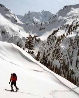 A skier ascends Ruth Mountain with Nooksack Tower and the summit of Mt. Shuksan in the distance.